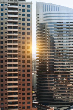 Foto de Un plano vertical de dos rascacielos residenciales modernos con patrones de fachadas de vidrio en una puesta de sol con una llamarada; vista de dos rascacielos de viviendas contemporáneas en un centro de la metrópoli en un amanecer - Imagen libre de derechos