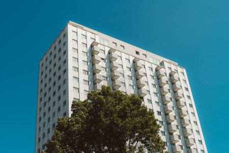 Téléchargez les photos : Capture d'un bâtiment dans des tons de blanc et de beige, à angle bas, les balcons forment des cubes qui émergent de l'intérieur du bâtiment, en face d'un arbre, et en arrière-plan le ciel bleu - en image libre de droit