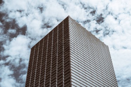 Foto de Una torre de negocios con una arquitectura contemporánea cuboide con ventanas horizontales rectangulares simétricas que forman un patrón de rayas, en un paisaje nuboso blanco dramático en un cielo de color gris - Imagen libre de derechos