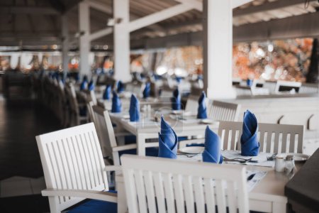 Foto de Una vista selectiva del foco en un ajuste de la mesa de la cena y los cubiertos en un restaurante tropical en las islas pacíficas; Los muebles se hacen de madera blanca y los cojines de las servilletas y de la silla del comedor son azules - Imagen libre de derechos