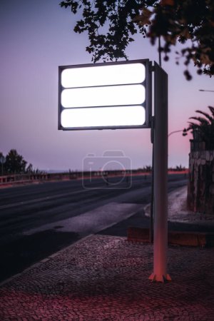 Téléchargez les photos : Une capture de mise au point sélective verticale de trois gabarits de panneaux de rue vides de couleur blanche sur le bord de la route du trottoir avec le coucher de soleil au crépuscule violet en arrière-plan - en image libre de droit
