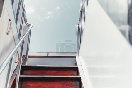 Téléchargez les photos : A shot captured from the lower deck when climbing a wooden stairway and shiny metallic railings leading to the upper deck of a white sailing yacht; on a warm sunny clear sky day in the Maldives island - en image libre de droit