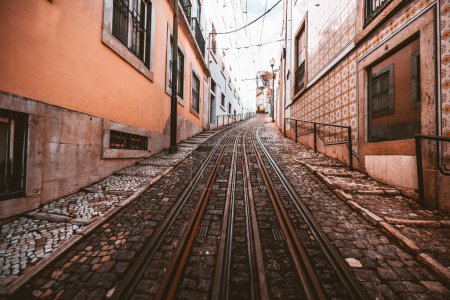Photo for A wide-angle view of a road with a retro two-lane tramway over paving stone on a narrow street in a picturesque old neighborhood in shades of salmon on the walls and tiles in Lisbon, Portugal - Royalty Free Image