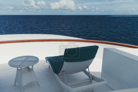 Téléchargez les photos : A wide-angle shot of an outdoor white recliner (from the back), with teal cushions on it, and a coffee table next to it on the upper deck of a luxury sailing yacht around the Maldives island - en image libre de droit