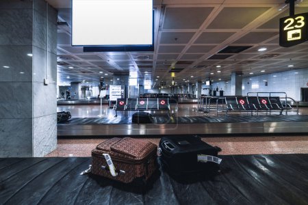 Téléchargez les photos : Several luggage wheeled suitcases are traveling on the baggage conveyor belts in an arrival area of a modern airport terminal with empty seat rows in the background and a screen mockup in a foreground - en image libre de droit