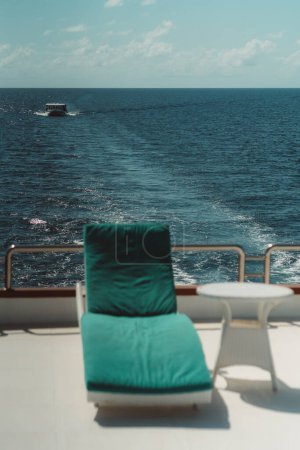 Téléchargez les photos : A vertical shot with a selective focus on the boat in the background: the upper deck of a diving yacht with a recliner and a coffee table in a defocused foreground; the speedboat at the distance - en image libre de droit