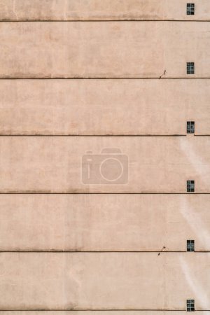 Photo for A vertical shot of a residential building wall with a sequence of small windows and floor separation lines on the plastered facade; a seamless texture of a house elevation with windows and stripes - Royalty Free Image
