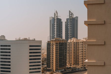 Photo for An urban landscape from the drone point of view with multiple modern residential high-rises and two bluish contemporary business office skyscrapers in the background rising above the Dubai desert dawn - Royalty Free Image