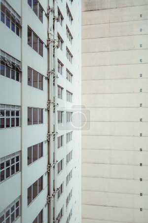 Téléchargez les photos : A vertical shot of a dwelling high-rise elevation with a pattern of small windows and stripes; a wide-angle view of a residential house facade with plastered walls, group of pipes, and rows of windows - en image libre de droit