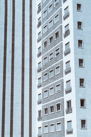 Téléchargez les photos : Vertical capturing of a high-rise residential building, focusing on a facade with horizontal detail painted in a dark gray color that is distinct from the light gray on which the apartment is painted - en image libre de droit