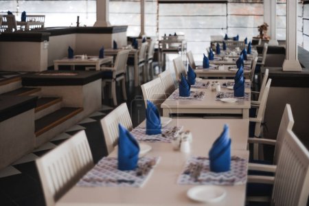 Foto de Enfoque selectivo en mesas y sillas de madera blanca, en un restaurante en la isla pacífica. Las mesas de la cena están vestidas con servilletas azules crujientes y limpiamente dispuestos de cubiertos. - Imagen libre de derechos