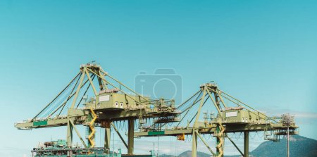 Téléchargez les photos : The capture of two massive yellow container handling cranes at work at the bustling dockside of Rio de Janeiro. These cranes stand tall, dominating the skyline as they expertly maneuver containers - en image libre de droit