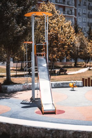Photo for Vertical capture on a playground surrounded by trees, a narrow swing, with ropes to climb up instead of the usual ladder to reach the top of the swing, on a bright and warm sunny day - Royalty Free Image