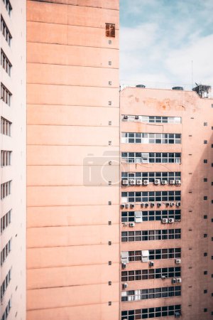 Téléchargez les photos : A vertical capture of an inner corner of two salmon-colored buildings for habitation with plenty of tiny squared windows, several outdoor air conditioning unit compressors visible on a sunny day - en image libre de droit