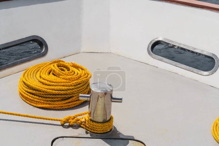 Foto de A close-up shot of a shiny bollard made of steel with a very long golden yellow stranded sailing/boating rope tied to it for mooring the yacht with white deck, still out at sea in the Maldives - Imagen libre de derechos