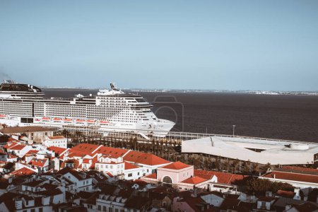 Téléchargez les photos : Un énorme bateau de croisière amarré dans la ville de Lisbonne, d'un côté une vue panoramique sur la bordure sud du fleuve Tejo, et de l'autre logement de Lisbonne au premier plan, par une belle journée de ciel bleu - en image libre de droit