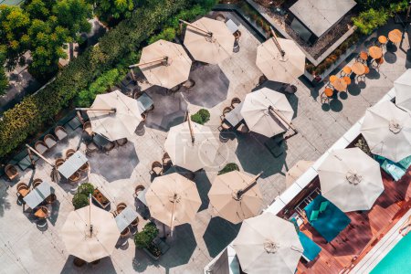 Foto de Top view from a drone of an outdoor bar with several open octagonal sunshades making a funny landscape, bordering one part of the terrace a garden, on the other side a lounge area in front of the pool - Imagen libre de derechos