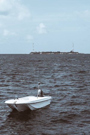 Foto de A stunning vertical shot of a white fishing boat tethered to another vessel, while the expansive seawater and a picturesque island dominate the background in selective focus. - Imagen libre de derechos