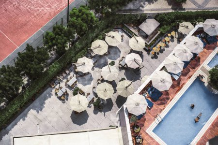 Foto de Top view from a drone of an outdoor bar with sunshades creating a beautiful landscape, adjacently a lounge and pool area with people resting, bordering the terrace trees hide the clay tennis court - Imagen libre de derechos