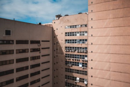 Foto de A capture of an inner corner of two peach-colored habitation apartments with several tiny squared windows, and many outdoor air conditioning unit compressors visible on a blue sky day due to the warm - Imagen libre de derechos