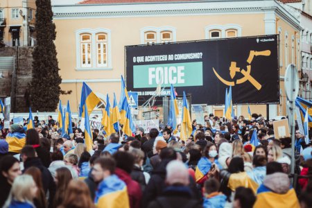 Foto de Lisboa, Portugal - 24 de febrero de 2023: Enfoque selectivo captura a una multitud apasionada de manifestantes contra la guerra, sosteniendo orgullosamente banderas ucranianas para conmemorar el primer aniversario del conflicto armado - Imagen libre de derechos