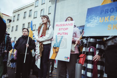 Téléchargez les photos : Lisbonne, Portugal - 24 février 2023 : Des femmes rassemblées pour protester contre la guerre, tenant le drapeau ukrainien et de puissants messages anti-guerre sur des banderoles marquant le premier anniversaire de la guerre en Ukraine - en image libre de droit