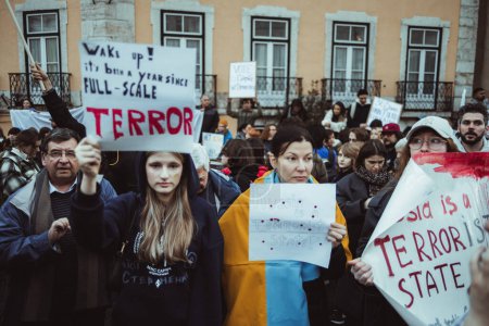 Téléchargez les photos : Lisbon, Portugal - February 24, 2023: In the front row of a protest marking the one-year anniversary of the conflict in Ukraine, some women in focus hold cardboards with powerful anti-war messages - en image libre de droit