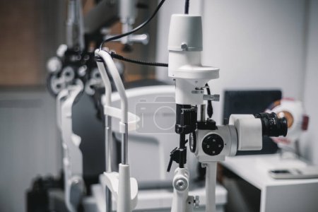 Téléchargez les photos : Le bureau d'ophtalmologie d'un médecin, avec une machine laser de photo-coagulation blanche au foyer et dans les environs, crée un environnement clinique stérile au premier plan. - en image libre de droit
