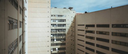 Téléchargez les photos : A panoramic of humble suburban apartments in Rio de Janeiro; their cream color radiates warmth and the square windows, each equipped with air conditioning, provide a glimpse into people's lives there - en image libre de droit