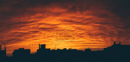 Téléchargez les photos : Vue panoramique d'un coucher de soleil orange vif, contrastant avec les silhouettes des bâtiments et des maisons de la ville ; le scénario poussiéreux enveloppe la ville d'une brume presque inhabituelle - en image libre de droit