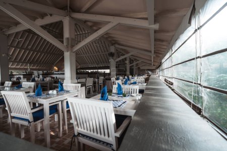 Photo for In the corner of the restaurant, our eyes are drawn to the pristine white tables and chairs made of wood, creating a soothing contrast against the dark blue accents of the napkins and chair cushions - Royalty Free Image