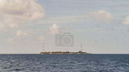 Téléchargez les photos : Du point de vue d'un bateau naviguant dans la vaste étendue de la mer, une vue sur une île lointaine. Sur fond de ciel magnifique peint en bleu, les silhouettes d'une végétation luxuriante - en image libre de droit