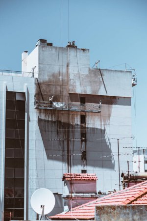 Photo for A vertical shot captures an apartment wall being cleaned; Blackened water drips down the building, creating a striking contrast against the white paint, the sky is clear blue - Royalty Free Image