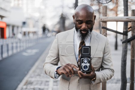 Photo for An aging man dressed elegantly holding an old TLR film camera. A selective focus adds depth, and copy space allows for customization. The shot is nostalgic, capturing a bygone era of photography. - Royalty Free Image