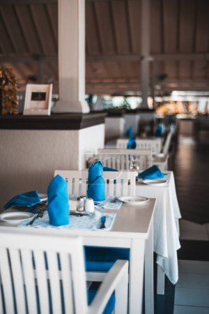 Foto de Maldivas; enfoque selectivo en mesas de comedor bien decoradas con servilletas plegadas azules, cubiertos y una placa sous azul, destacando la atención al detalle y la sofisticación del entorno. - Imagen libre de derechos