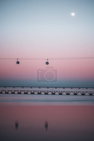Photo for Lisbon; A low-key, vertical view of a beautiful scene featuring a full moon, pink sky sunset, the Tejo river, and a cable car. The overall effect is a serene and dreamy magical scene - Royalty Free Image