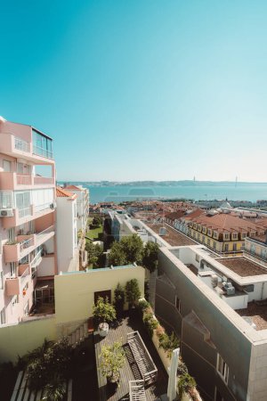 Foto de Lisboa; vertical; gran angular; una vista desde un apartamento con una fachada de color salmón a la ciudad, que muestra el río Tejo y la réplica del puente Golden Gate en la distancia - Imagen libre de derechos