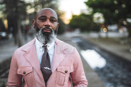 Photo for Lisbon; Selective focus on a bald man with a stylish beard posing for a close-up portrait; wears a pink jacket, white shirt, and polka dot tie. looks very charming, handsome, and pensive; copy space - Royalty Free Image