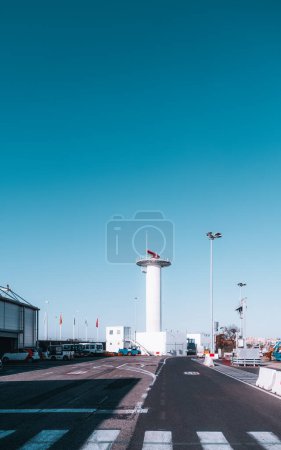 Photo for A vertical shot of Lisbon's airport area, a white control tower in the background. In the front, a road with official vehicles and gangways, and zebra crossing for the bustling workers - Royalty Free Image