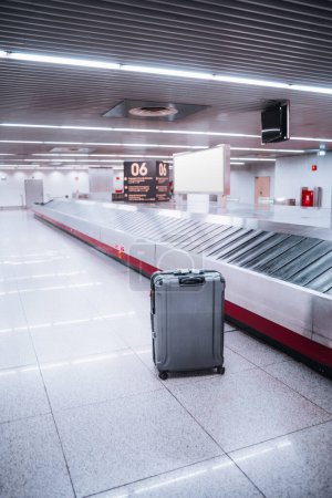 Téléchargez les photos : Aéroport de Lisbonne ; plan vertical ; mise au point sélective sur un seul sac dans la zone de récupération des bagages, debout contre le sol gris. Le cadre intérieur avec des lumières blanches ajoute à l'atmosphère - en image libre de droit