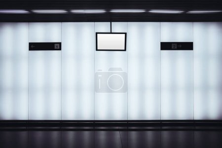 Foto de En un moderno pasillo de la estación de metro de Lisboa, una maqueta de pantalla LCD en blanco se encuentra entre dos punteros direccionales. La escena monocromática emana un ambiente elegante con sus tonos de blanco y negro - Imagen libre de derechos