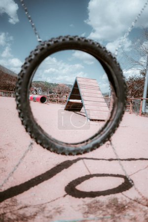 Photo for Vertical shot of a dog playground; A tire in the foreground frames the scene, revealing a wooden ramp beyond it. The vibrant blue sky adorned with fluffy white clouds creates a striking contrast - Royalty Free Image