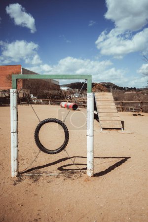 Photo for A vertical shot, in Barcelona, a canine park with sandy ground and agility training equipment. A dog jump tire and wooden ramp in the background provide interactive play for our furry friends - Royalty Free Image
