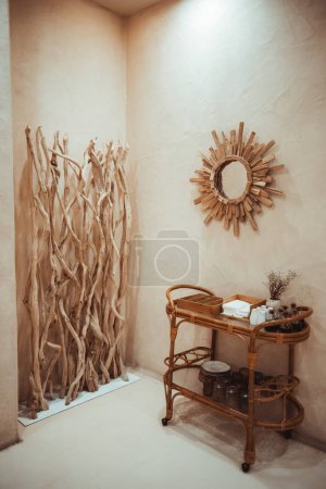 Téléchargez les photos : Plan vertical d'une maison rustique à Barcelone. Les murs beiges, les éléments en bois et le miroir créent de la chaleur. Une table basse en rotin avec des objets décoratifs et des herbes ajoutent une touche naturelle, un bel éclairage - en image libre de droit