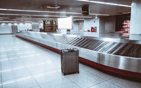 Téléchargez les photos : Aéroport de Lisbonne ; accent sélectif sur un seul sac dans la zone de récupération des bagages, debout contre le sol gris. Le cadre intérieur avec des lumières blanches ajoute à l'atmosphère - en image libre de droit
