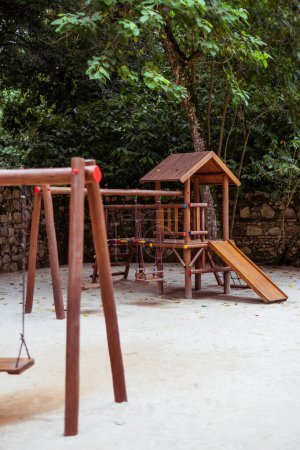 Vertical view of a kids playground embraced by lush tropical flora. A wooden slide and swing grace the scene, set against a sandy floor, creating a paradise for young adventurers