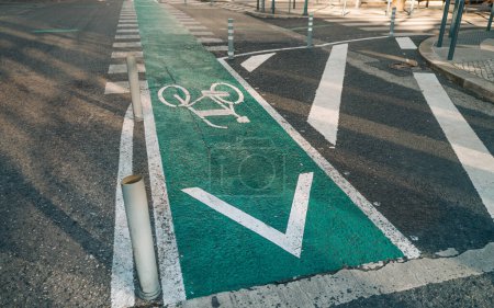 A dedicated green bike lane marked with white bike symbol and directional arrow, separated from the main road by white dashed lines and poles, promoting safe cycling in urban areas