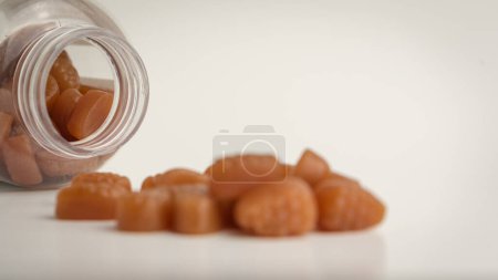 Foto de Gomitas de biotina para el cabello, la piel y las uñas que salen de la botella, exhibidas sobre un fondo blanquecino suave. - Imagen libre de derechos