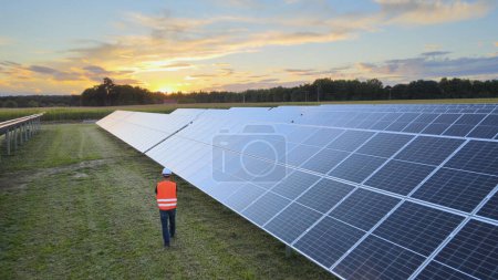 Photo for Aerial drone view following a Technician at work on a solar farm, during sunset - Royalty Free Image