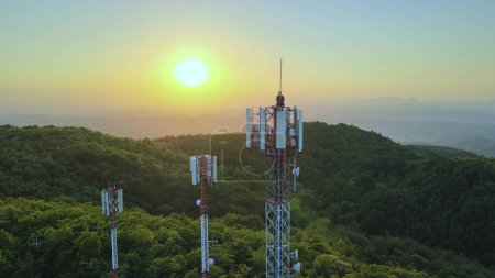 Photo for Aerial Of Technician Sitting On Top Of Telecommunications Tower At Sunset In The Mountain With Green Forest - Royalty Free Image